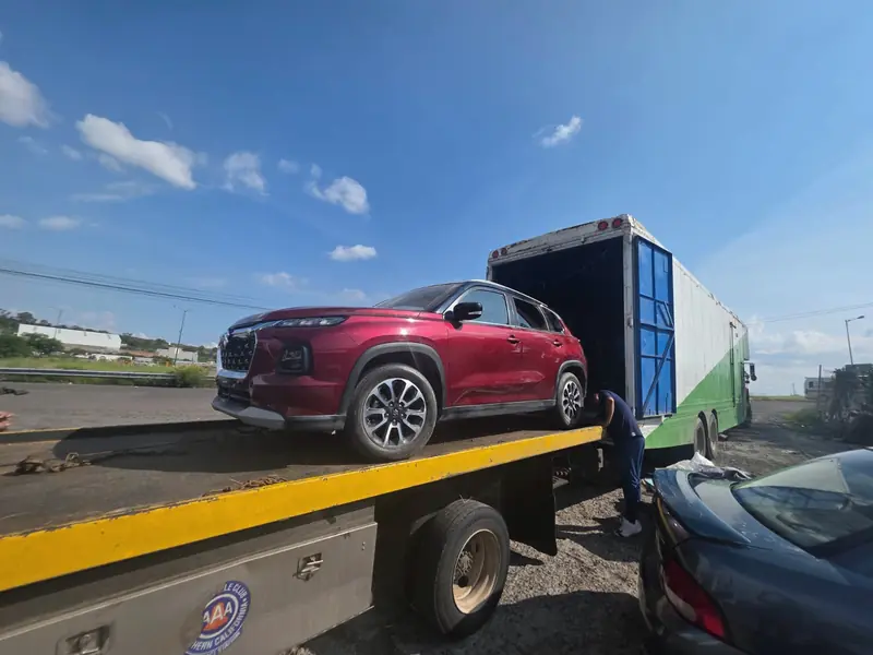 Camioneta roja subida a una grúa de plataforma, junto a un camión de Express Rico